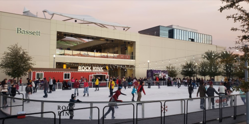 A lively outdoor ice skating rink at dusk, with people skating and a food truck nearby, surrounded by palm trees.