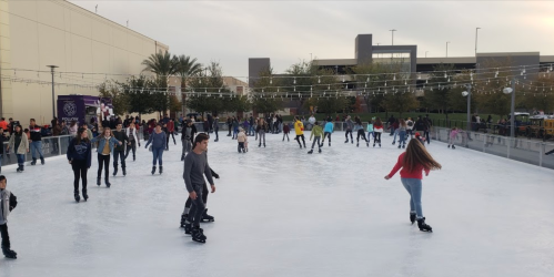A busy outdoor ice skating rink with people of all ages skating and enjoying the winter atmosphere.