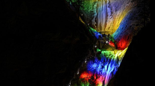 A colorful illuminated waterfall cascading down a rocky cliff in a dark setting.