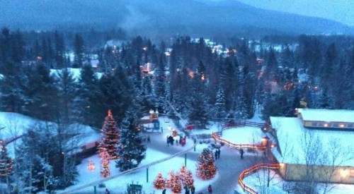 A snowy landscape with decorated Christmas trees, people walking, and twinkling lights in a winter wonderland setting.