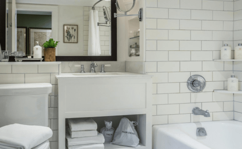 A modern bathroom featuring white subway tiles, a sink with a mirror, a bathtub, and neatly arranged towels.