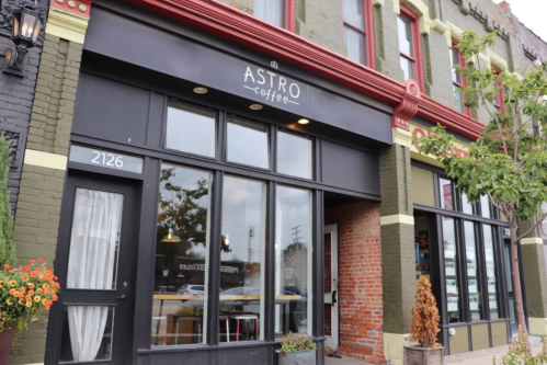 Exterior of Astro Coffee shop featuring large windows, a black awning, and colorful brick walls.