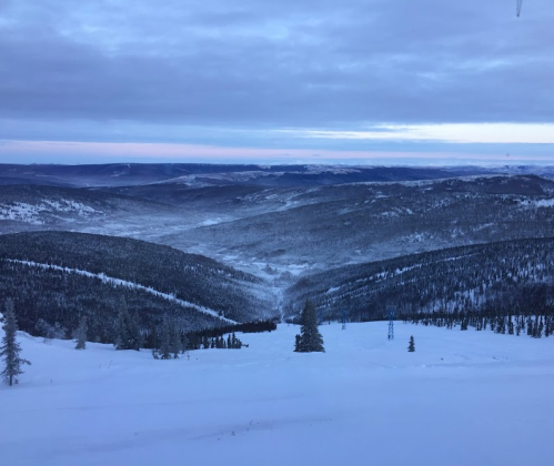 A snowy mountain landscape with rolling hills and a valley, under a cloudy sky.