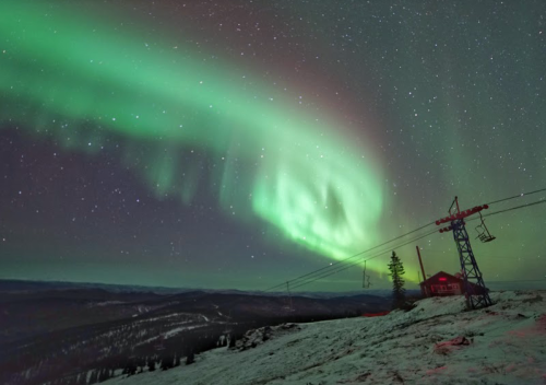 A vibrant aurora borealis illuminates the night sky above a snowy landscape and ski lift. Stars twinkle in the background.