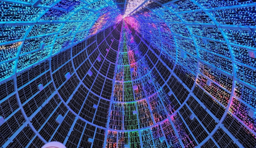 A colorful display of lights arranged in a spiral pattern, viewed from below, creating a vibrant, festive atmosphere.