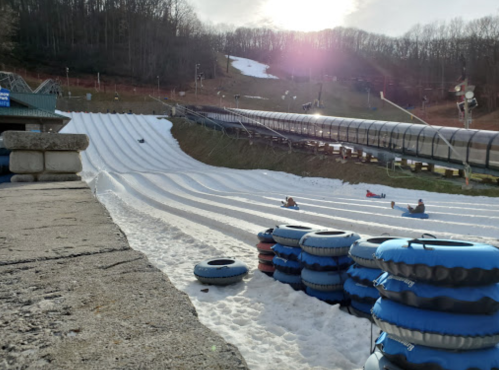 A snow tubing slope with several blue inner tubes stacked, and people tubing in the distance under a sunny sky.