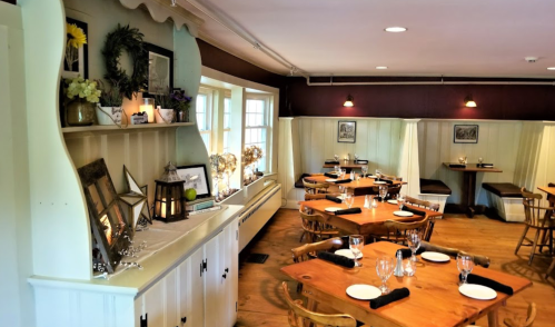 Cozy restaurant interior with wooden tables, chairs, and decorative shelves, creating a warm dining atmosphere.