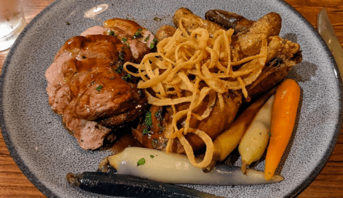 A plate featuring roasted meat, crispy onions, and colorful baby carrots on a textured gray plate.