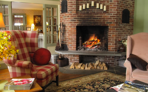 Cozy living room with a brick fireplace, two armchairs, and a warm fire, surrounded by decorative elements and a rug.