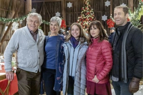 A group of five people smiling together in a festive barn decorated for the holidays.
