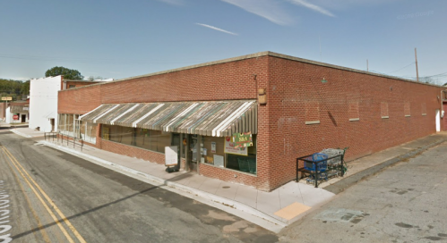 A brick building with a striped awning, located at a street corner, featuring a shopping cart outside.