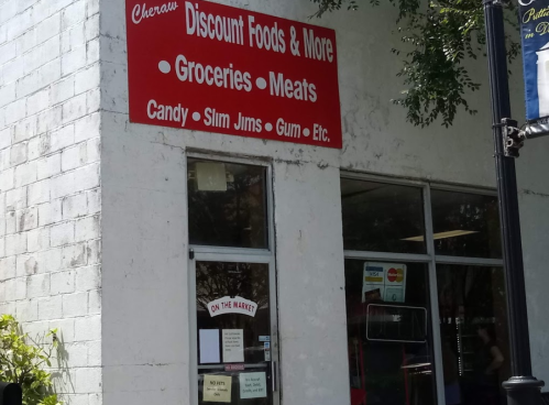 Storefront of "Cheraw Discount Foods & More," featuring a red sign listing groceries, meats, and snacks.