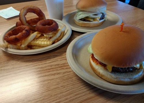 Two burgers with lettuce and cheese, and a plate of onion rings and fries on a wooden table.