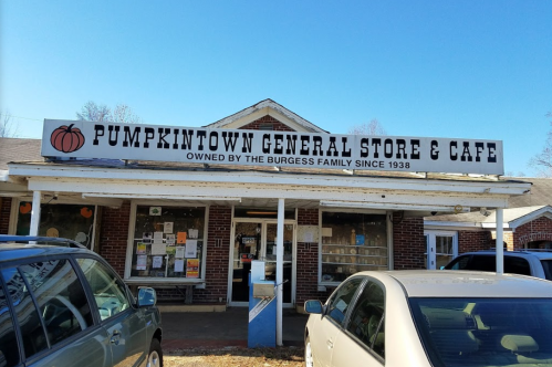 Exterior of Pumpkintown General Store & Café, featuring a sign and parked cars in front on a clear day.