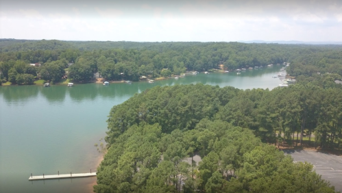 Aerial view of a serene lake surrounded by lush green trees and a dock, with boats moored along the shoreline.