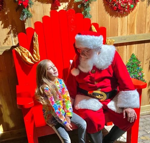 A young girl smiles at Santa Claus while sitting on a bright red chair decorated for the holidays.