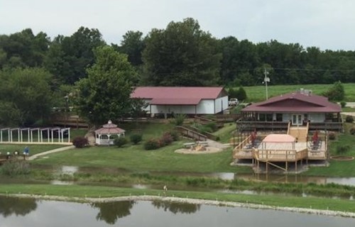 A scenic view of a property with a house, gazebo, and pond, surrounded by lush greenery and trees.