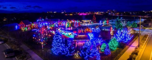 A vibrant display of colorful holiday lights illuminating a park at night, with trees and decorations glowing.