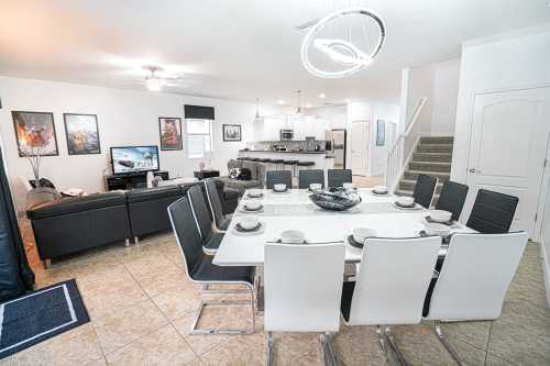 Modern dining area with a large table set for ten, open to a living space with a TV and kitchen in the background.