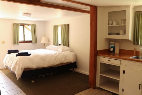 Cozy room with a bed, green curtains, and a kitchenette featuring a sink and shelves.