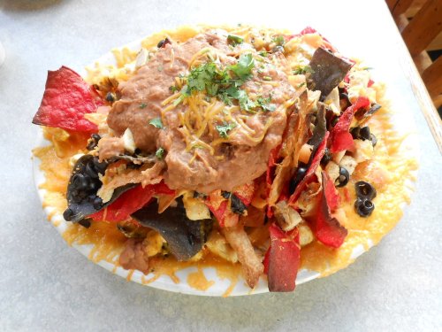 A colorful plate of nachos topped with beans, cheese, olives, and fresh herbs on a bed of tortilla chips.