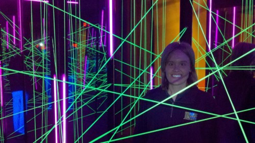 A person smiles in a dark room filled with vibrant green laser beams and colorful lights.