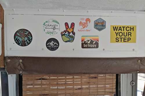 A wall with various colorful stickers and a caution sign that reads "WATCH YOUR STEP."