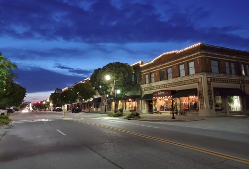 A quiet street at dusk, lined with charming buildings and warm lights under a blue sky.