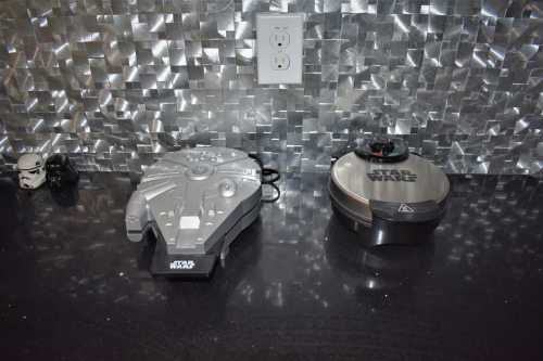 A countertop featuring a Millennium Falcon toy and a Star Wars-themed item against a metallic backsplash.