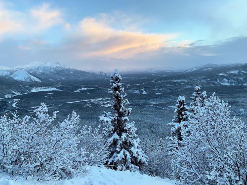 A snowy landscape with mountains in the distance, under a pastel sky, showcasing a serene winter scene.