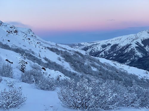 A serene winter landscape with snow-covered mountains and valleys under a pastel sky at dusk.