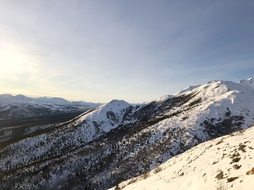 Snow-covered mountains under a clear sky, with a valley stretching between the peaks in the distance.