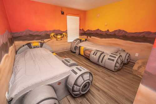 A themed bedroom with two beds designed to look like futuristic vehicles, set against a colorful desert mural.