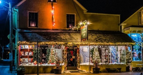 A festive shop decorated with Christmas lights and trees, glowing warmly at night.