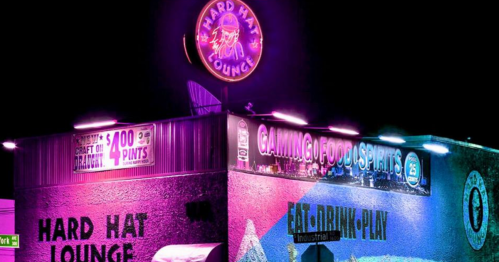 Neon-lit exterior of Hard Hat Lounge at night, featuring signs for gaming, food, and $4 pints.