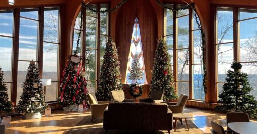 Cozy interior with large windows, decorated Christmas trees, and a festive atmosphere overlooking a scenic view.