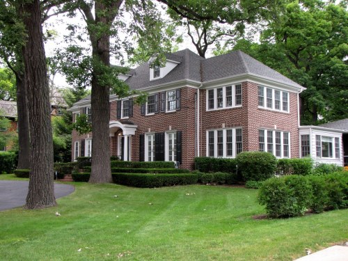 A large brick house with multiple windows, surrounded by green lawns and trees.