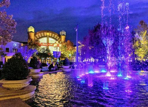 A vibrant fountain with colorful lights in front of a building, surrounded by trees at dusk.