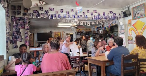 A busy restaurant interior with people dining, colorful decorations, and photos hanging from the ceiling.