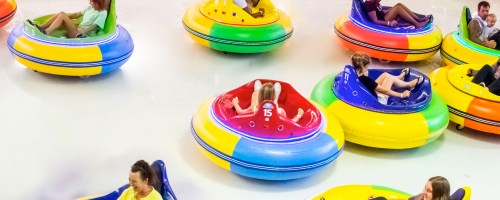 A colorful bumper car arena with people enjoying rides in vibrant, circular bumper cars.