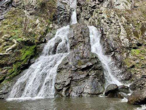 A serene waterfall cascading over rocky terrain, surrounded by lush greenery and a calm pool at the base.