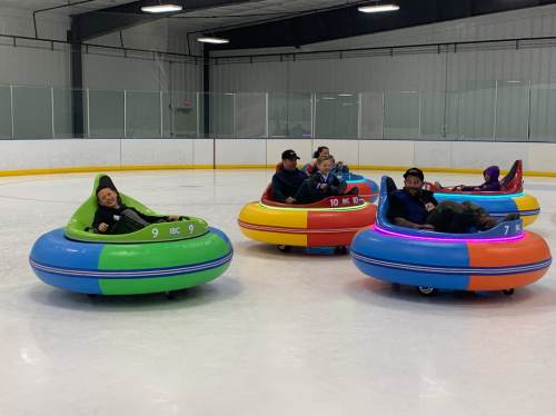 A group of people enjoying bumper cars on an ice rink, with colorful vehicles and a playful atmosphere.