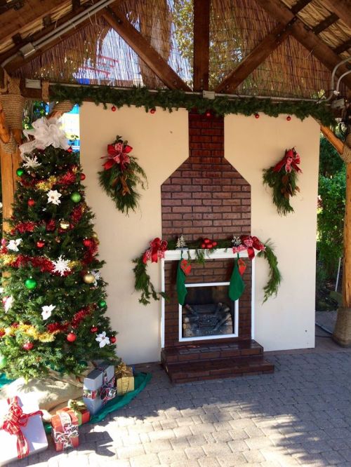A festive scene featuring a decorated Christmas tree, stockings, and a brick fireplace adorned with holiday greenery.