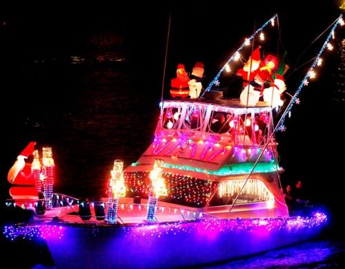 A brightly lit boat decorated with festive lights and Santa figures, sailing on dark water at night.