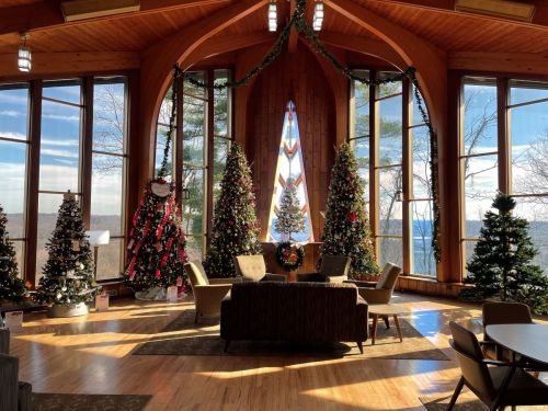 Cozy interior with large windows, decorated Christmas trees, and festive decor, overlooking a scenic winter landscape.