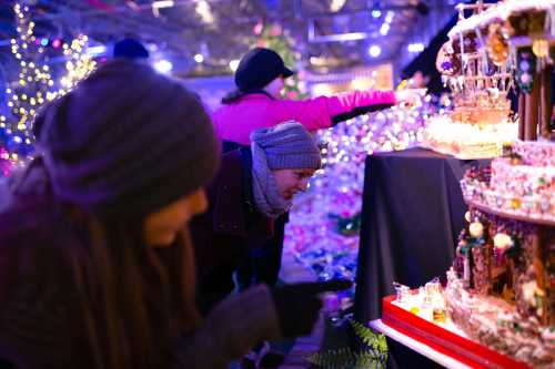 Two people admire a festive display of gingerbread houses, surrounded by colorful holiday lights.