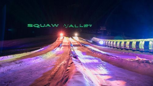 Colorful lights illuminate snowy slopes at Squaw Valley, with a ski lift visible in the background at night.