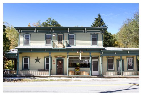 A two-story green building with a star decoration, featuring a porch and large windows, set against a clear blue sky.