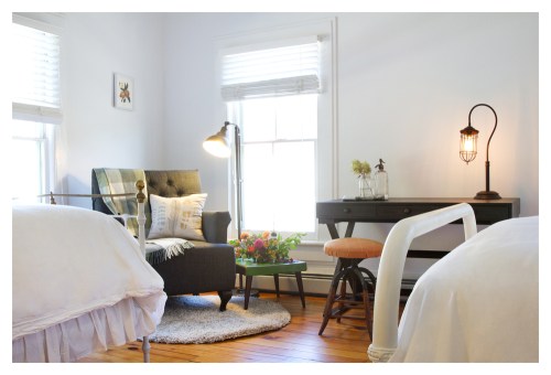 Cozy bedroom with two beds, a reading chair, a desk, and natural light from windows, featuring floral decor.