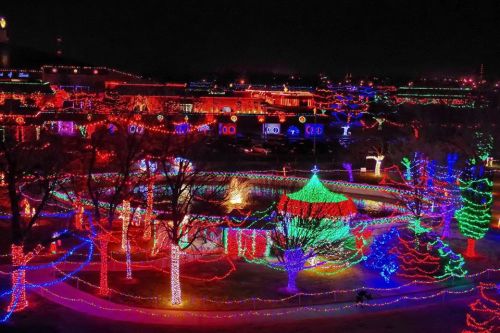 A vibrant display of colorful holiday lights illuminating a park at night, featuring trees and festive decorations.